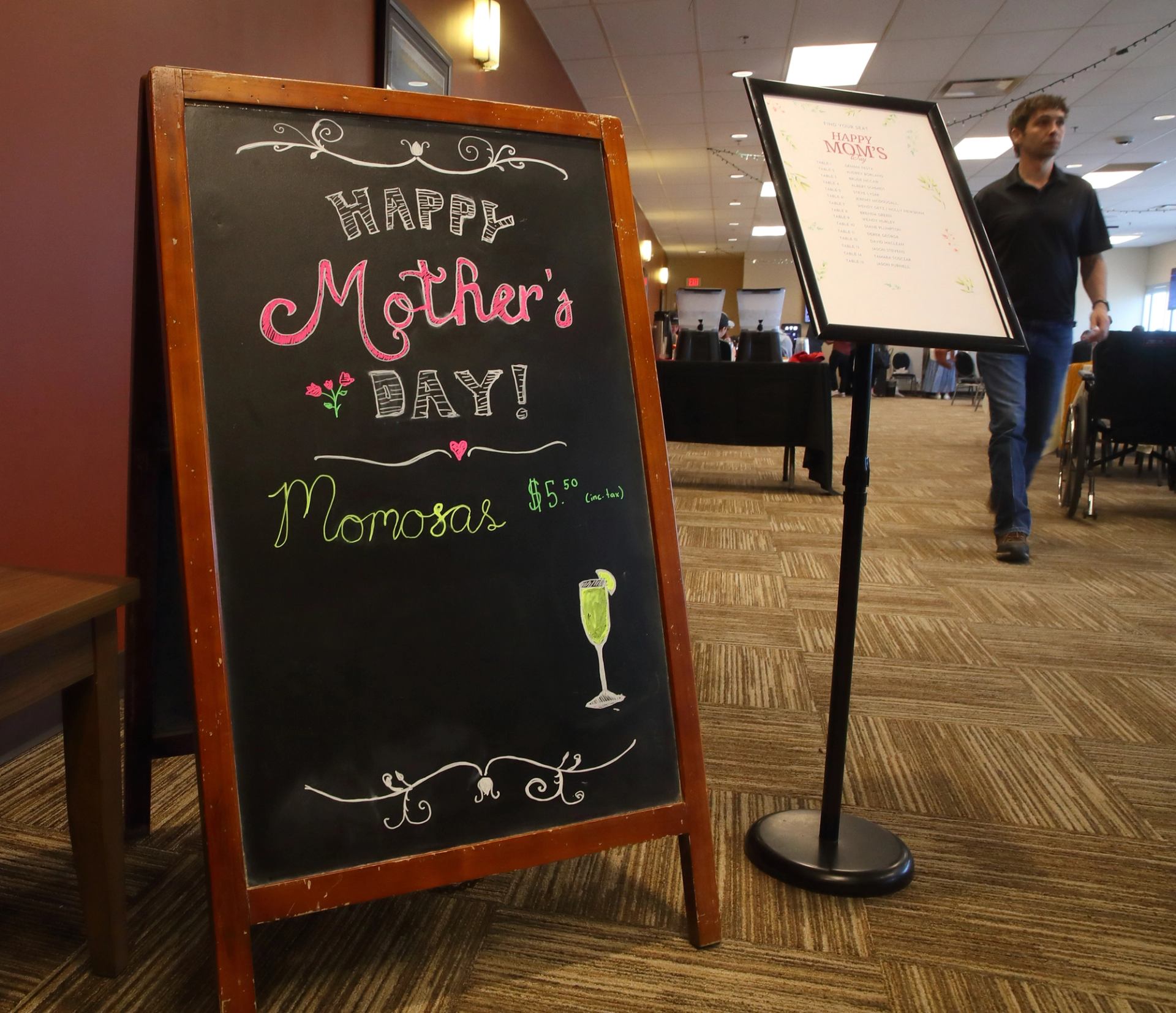 Chalkboard sign reading “Happy Mother’s Day! Mimosas $5” next to a menu stand in a dining area.