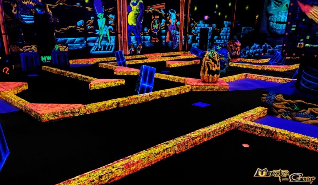 Glow-in-the-dark mini-golf course with neon obstacles and Monster Mini Golf logo.