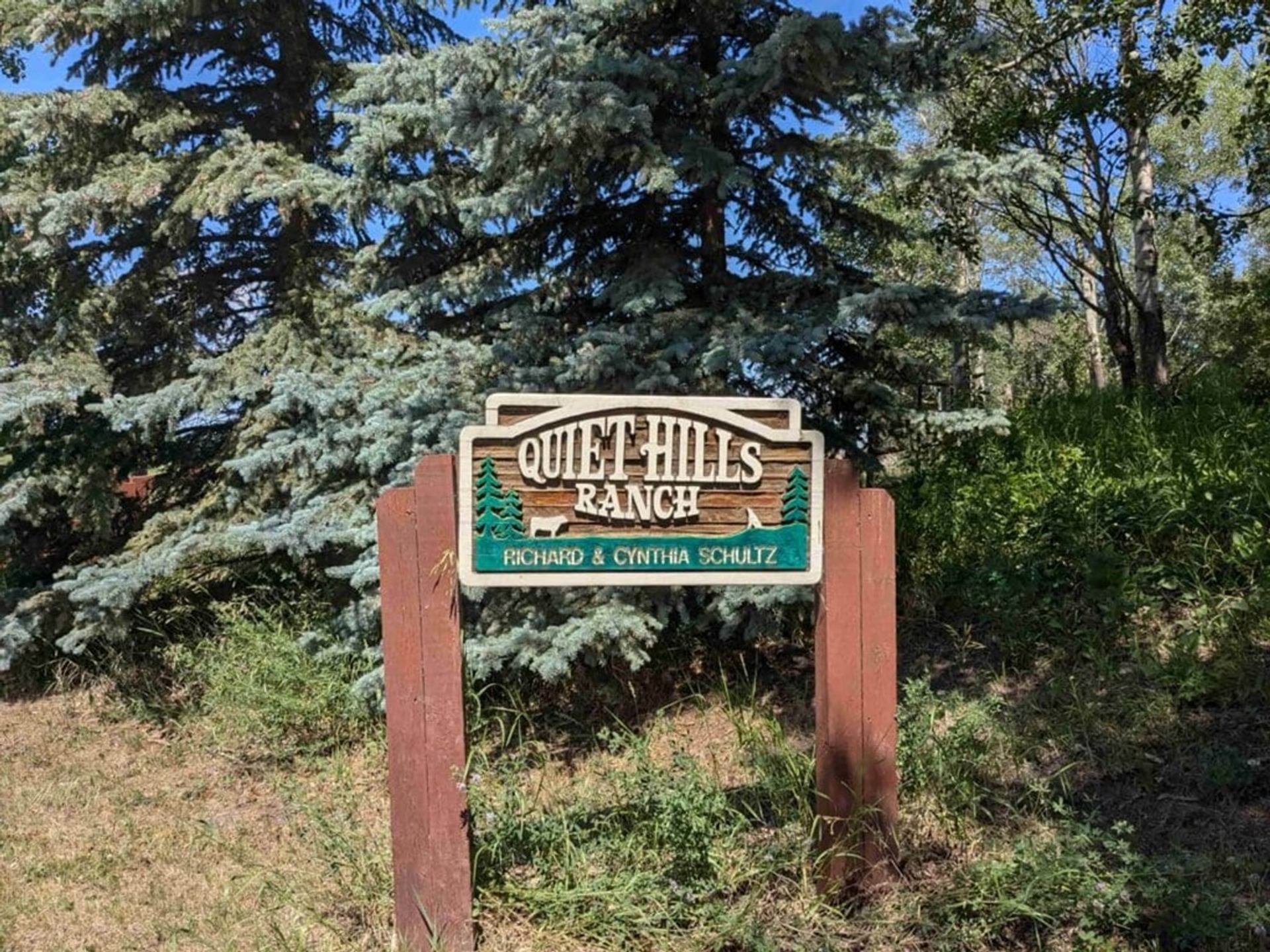 Wooden Quiet Hills Ranch sign with trees and grass in the background.