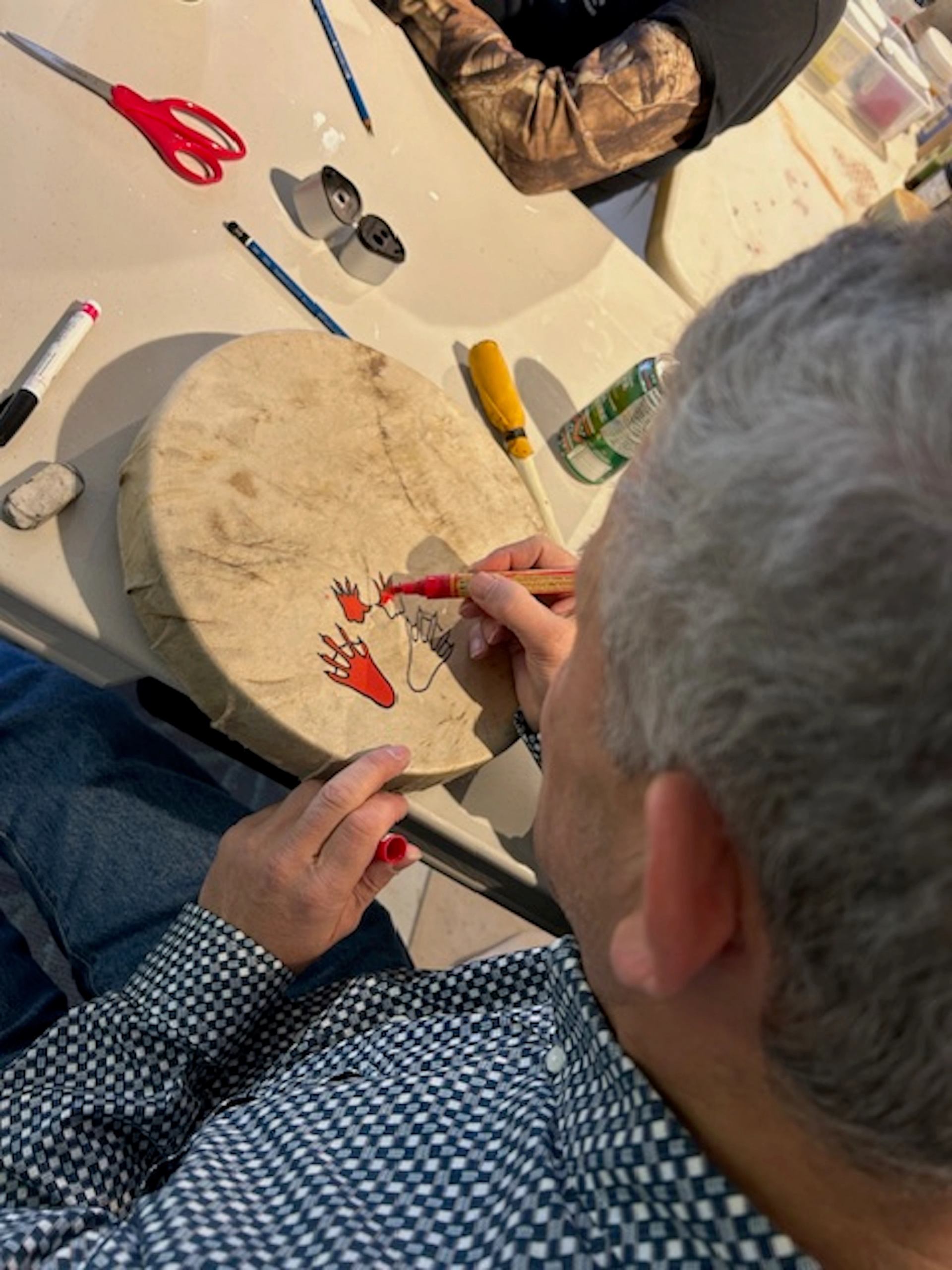 Person crafting with red scissors and paper at a workshop table.