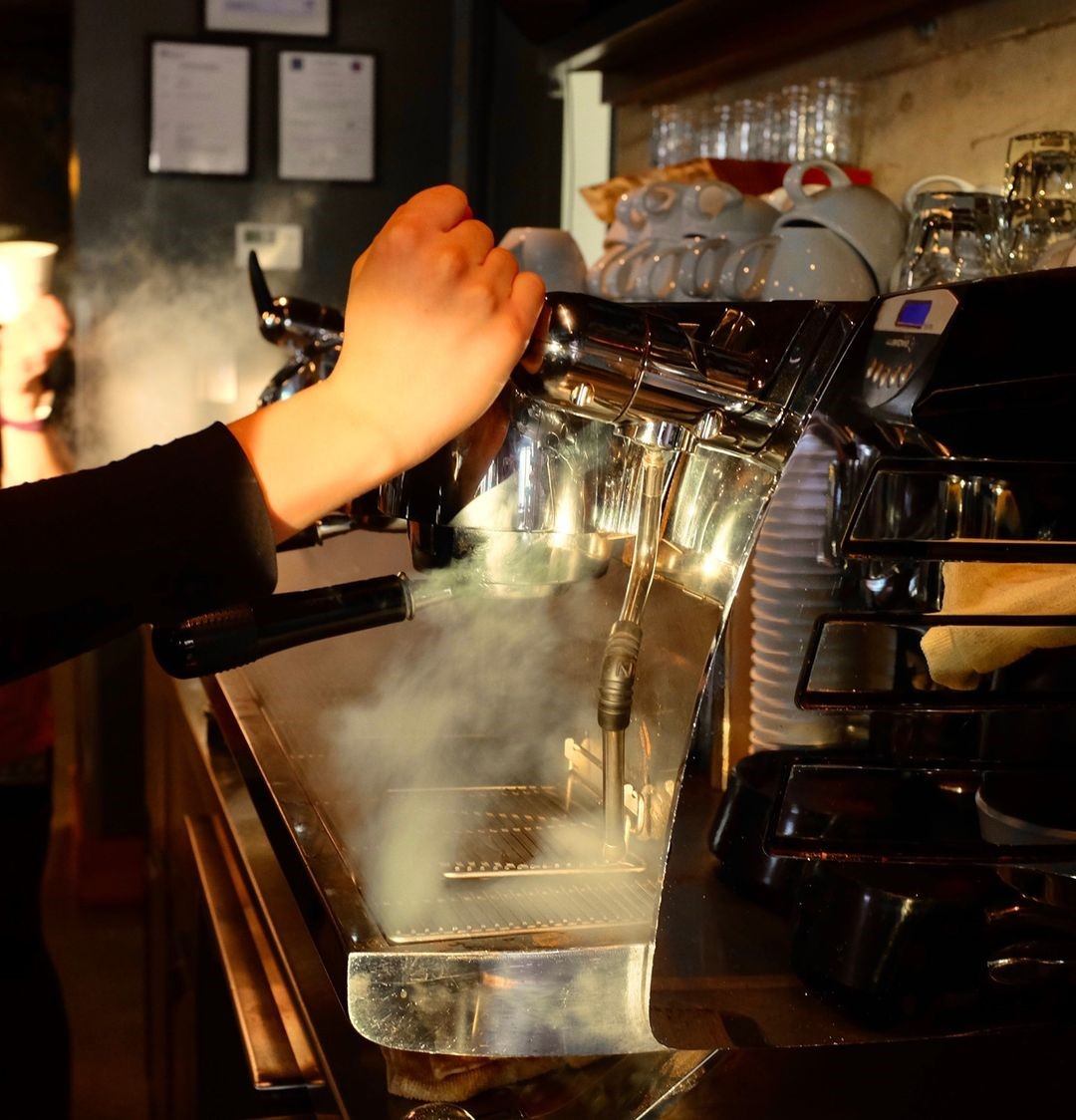 Barista using espresso machine with steam rising at Transcend Coffee.