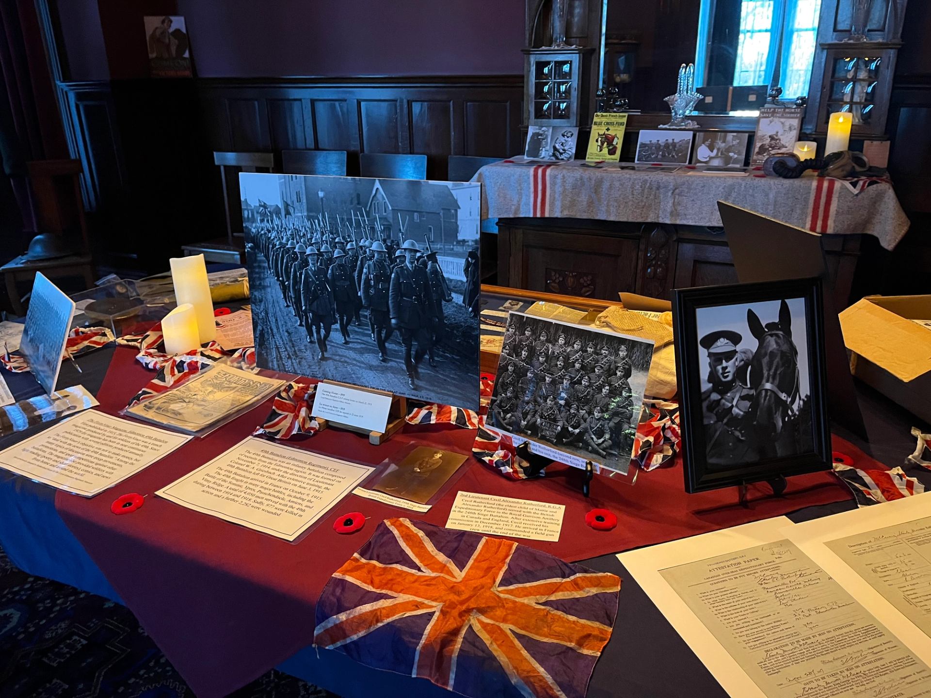 Museum display table with framed photos, documents, candles, and a Union Jack cloth.