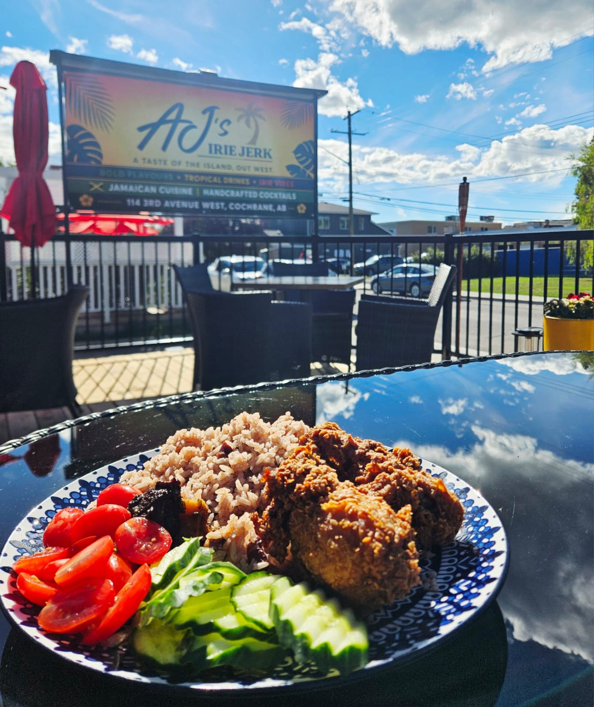 Plate of jerk chicken, rice, tomatoes and cucumber on AJ's Irie Jerk patio.