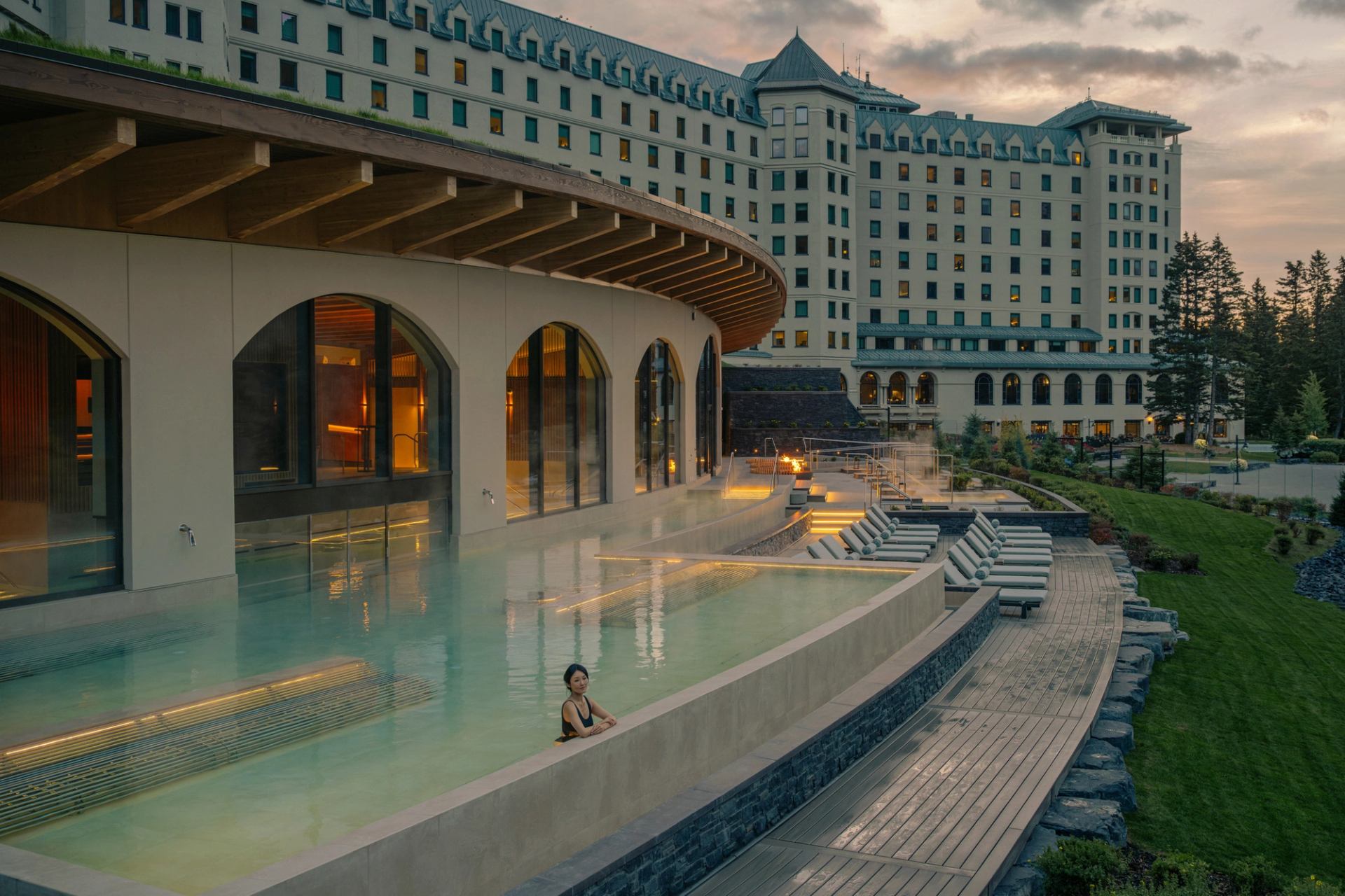 Outdoor infinity pool beside large hotel building with lounge chairs and landscaped gardens.