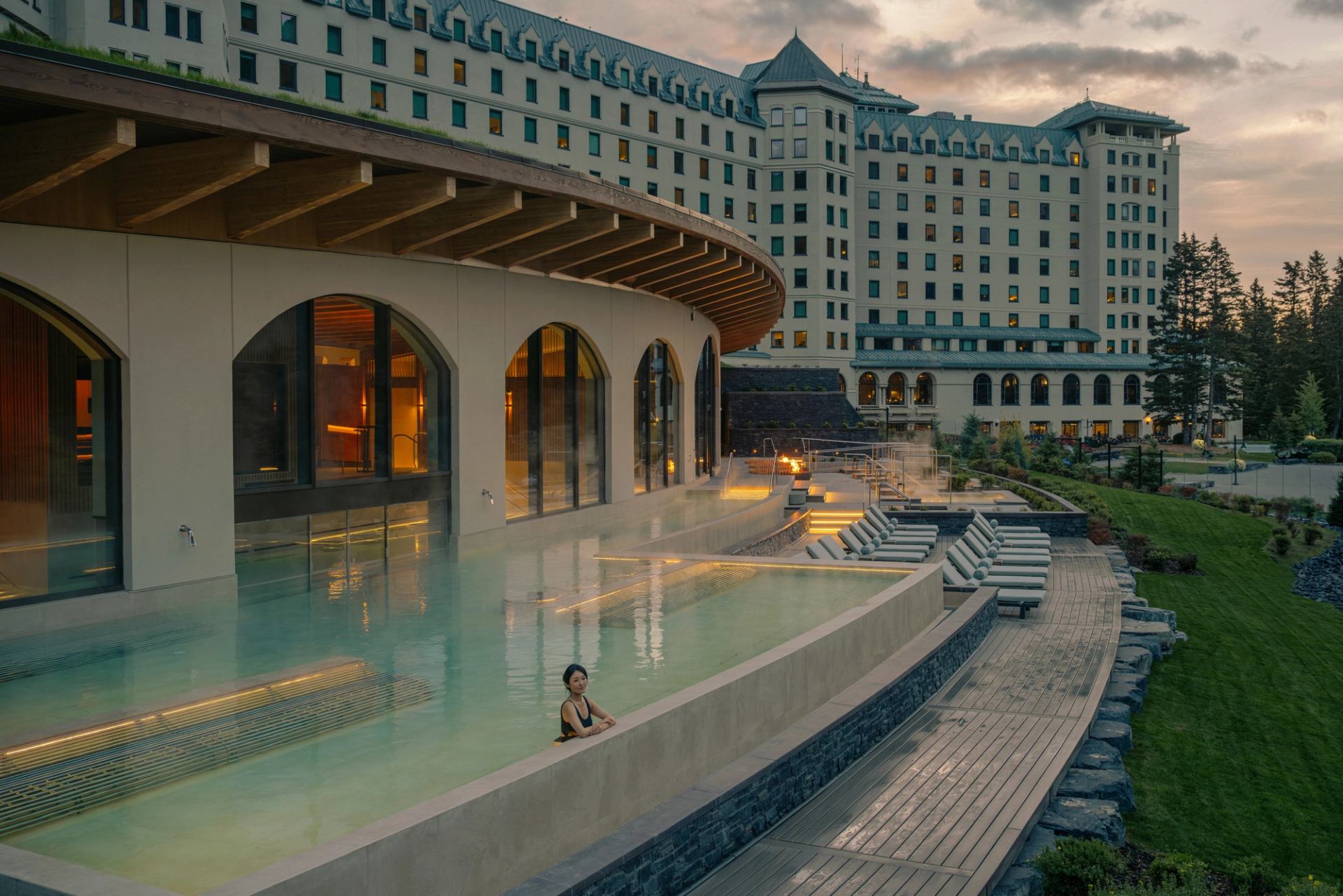 Outdoor infinity pool beside large hotel building with lounge chairs and landscaped gardens.