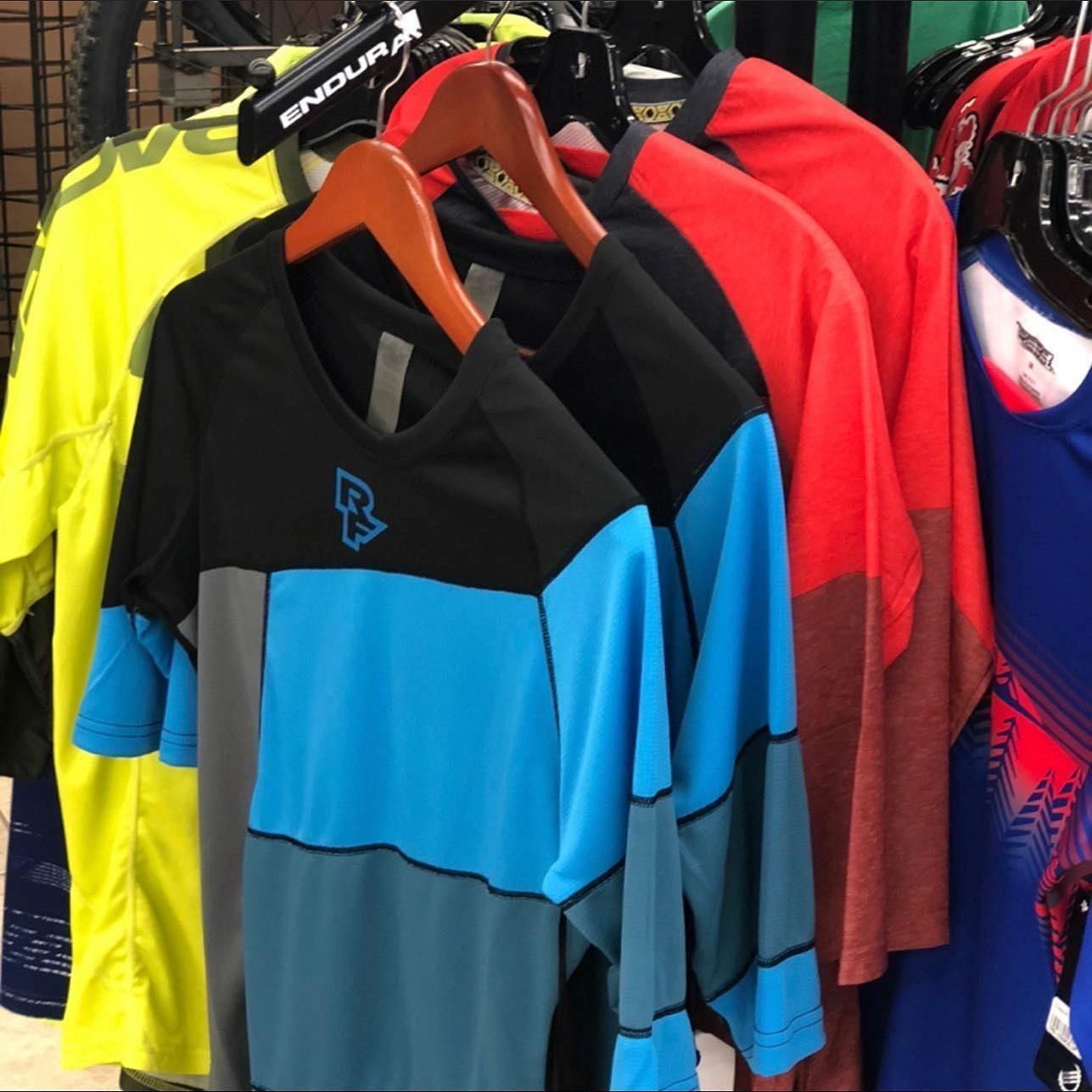 Hanging motocross jerseys on clothing racks, with yellow, black, blue, and red shirts visible.