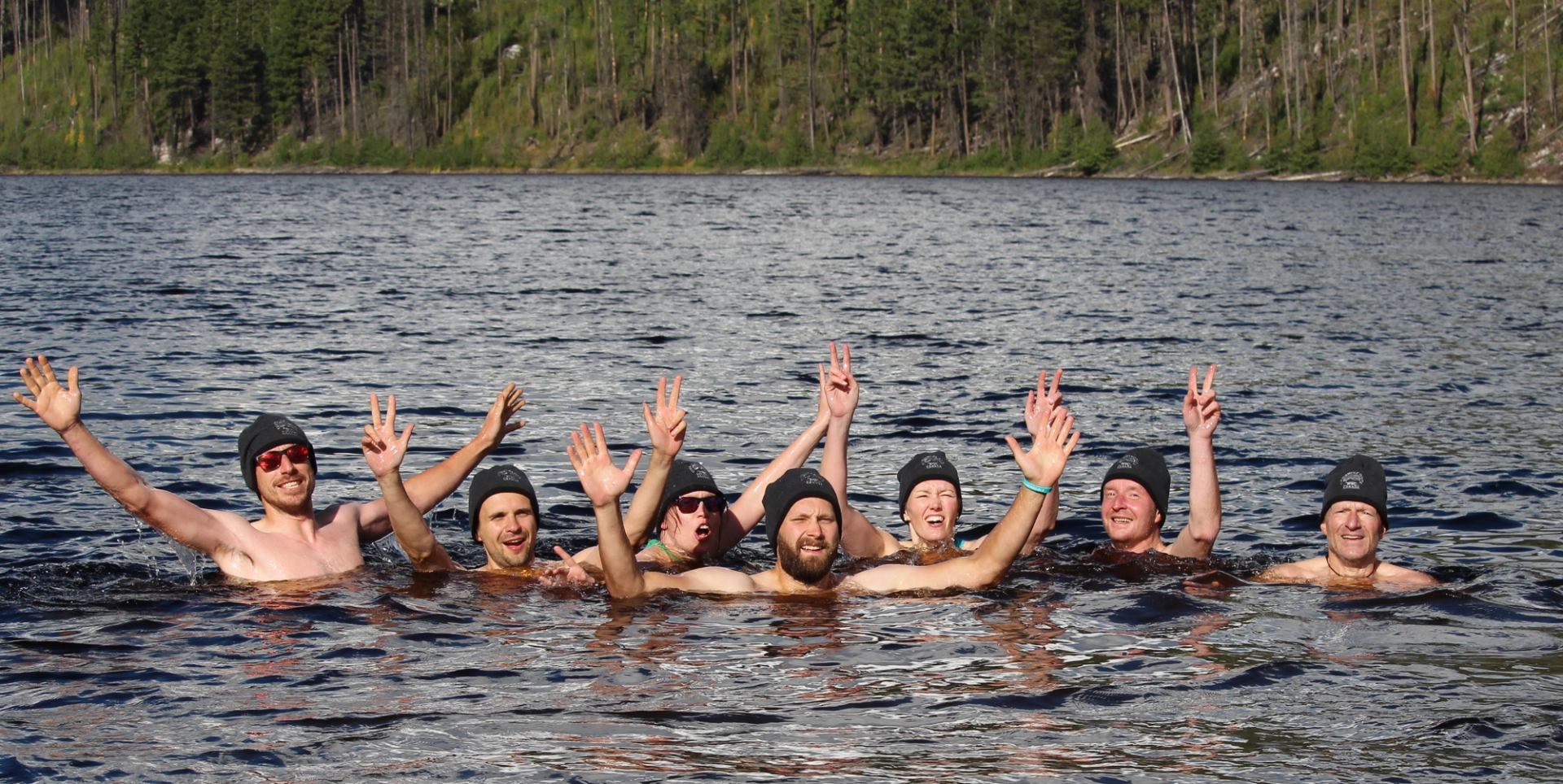 Hiking group taking a break and all together swimming in a lake with their hands in the air.
