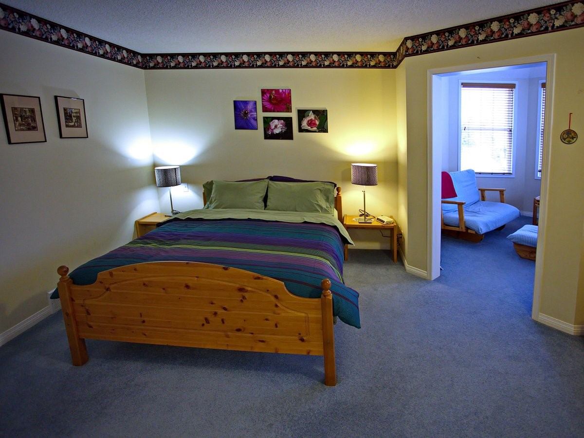 Cozy bedroom with a wooden bed, colorful bedding, and a small sitting area in the corner.