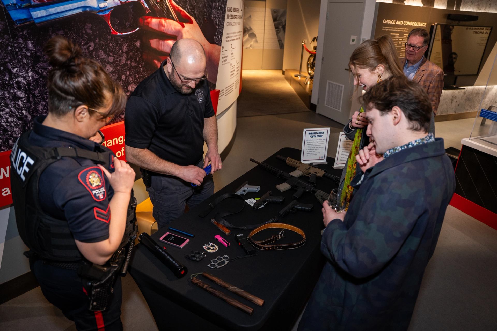 Police officer and visitors examine weapons displayed on a museum table.