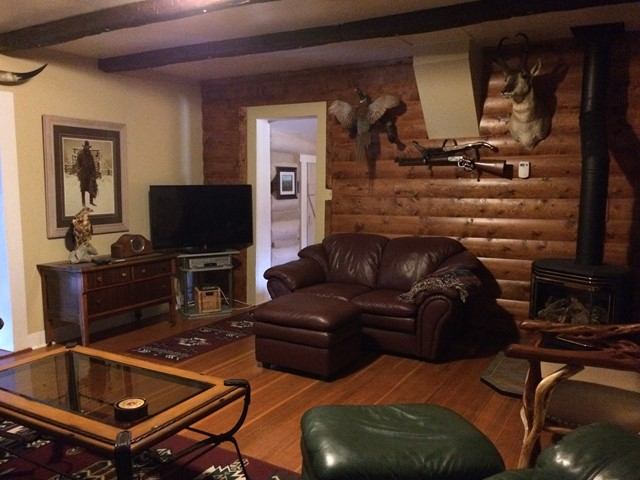 Rustic cabin living room with leather seating, wood stove, log walls, and western-style decor.