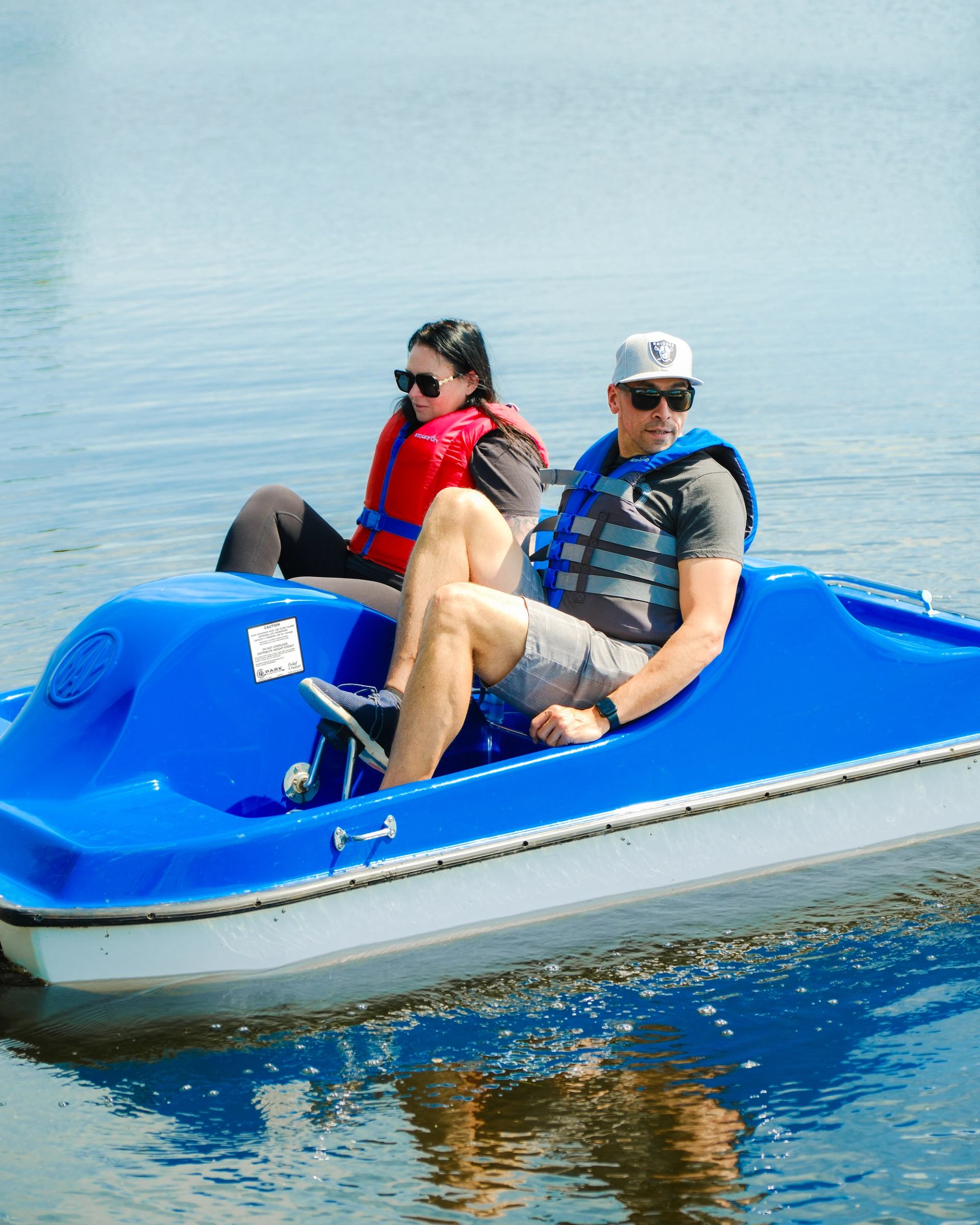 Two people in a blue pedal boat on calm water, wearing life jackets.