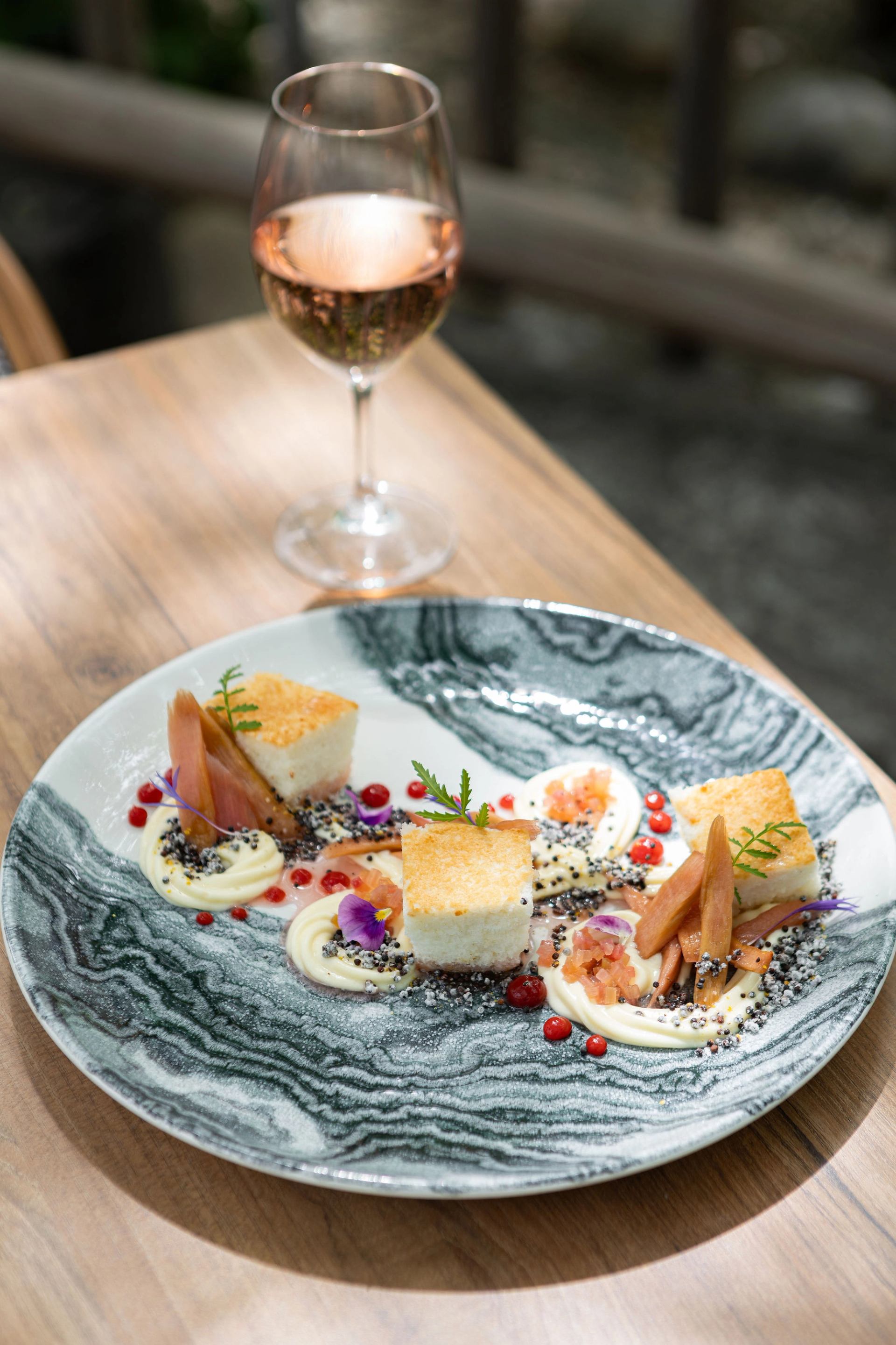 Plated dish with savoury cubes, vegetables, edible flowers and a glass of rosé.