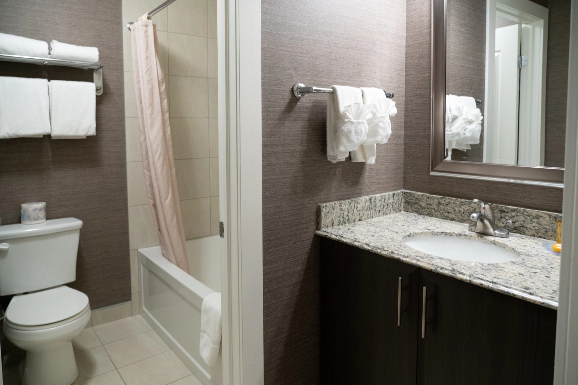 Clean hotel bathroom with granite sink, mirror, and pink shower curtain.