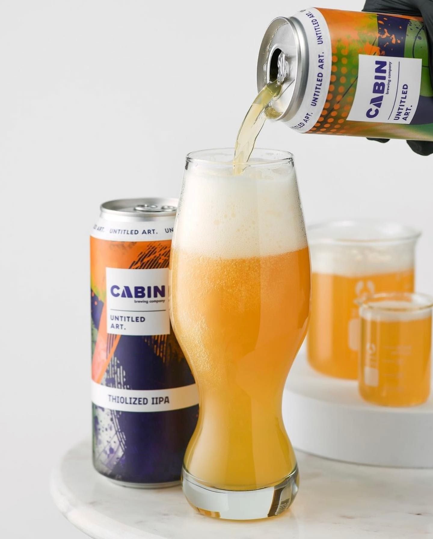 Beer can and glass with beer pouring, Cabin Brewing Company label visible.