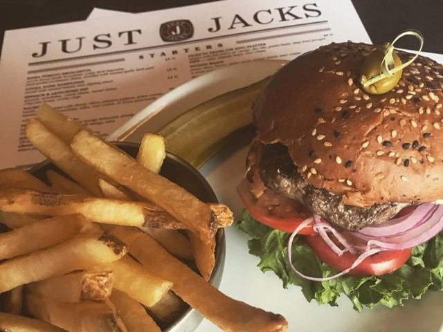 Gourmet burger with fries served on a plate beside a Just Jacks menu.