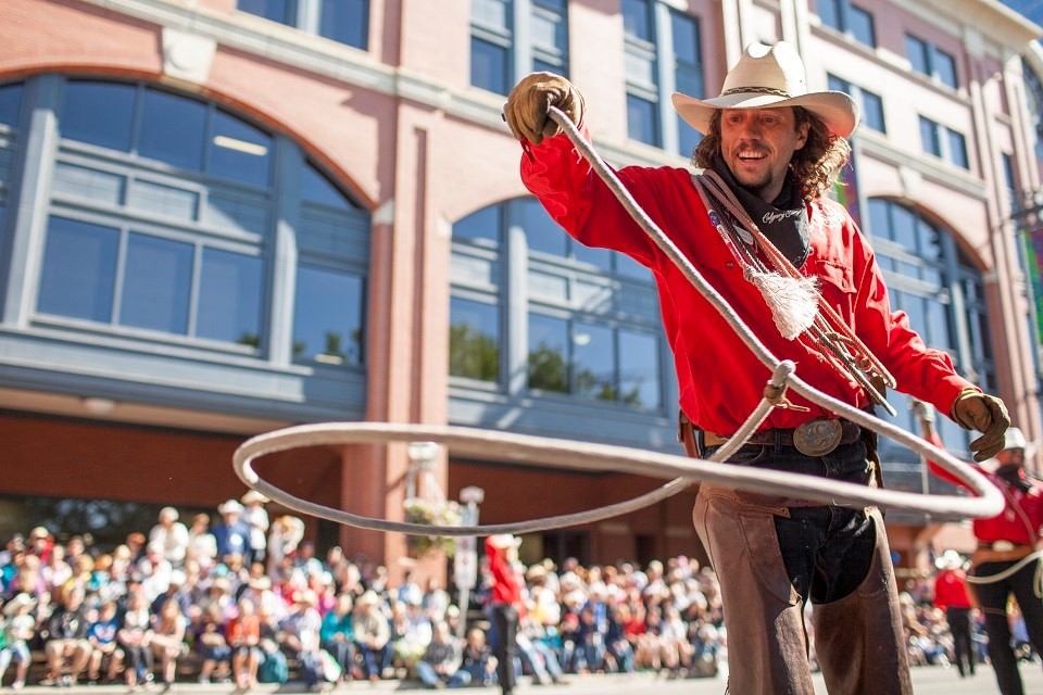 Performer in cowboy attire twirling a lasso at Calgary Stampede parade.