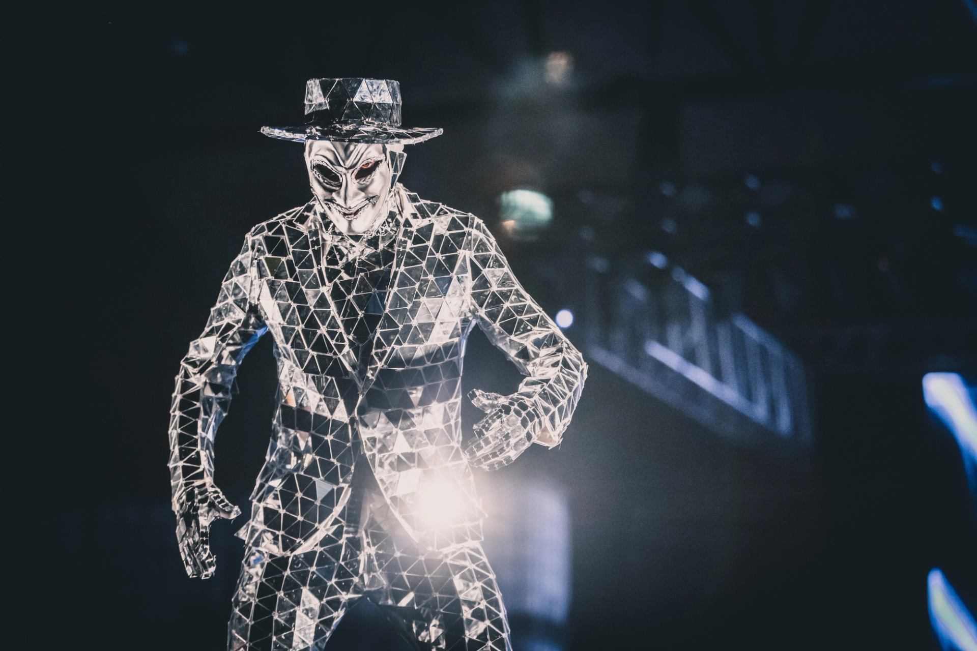 A masked glowing figure reflects light in a dimly lit room.