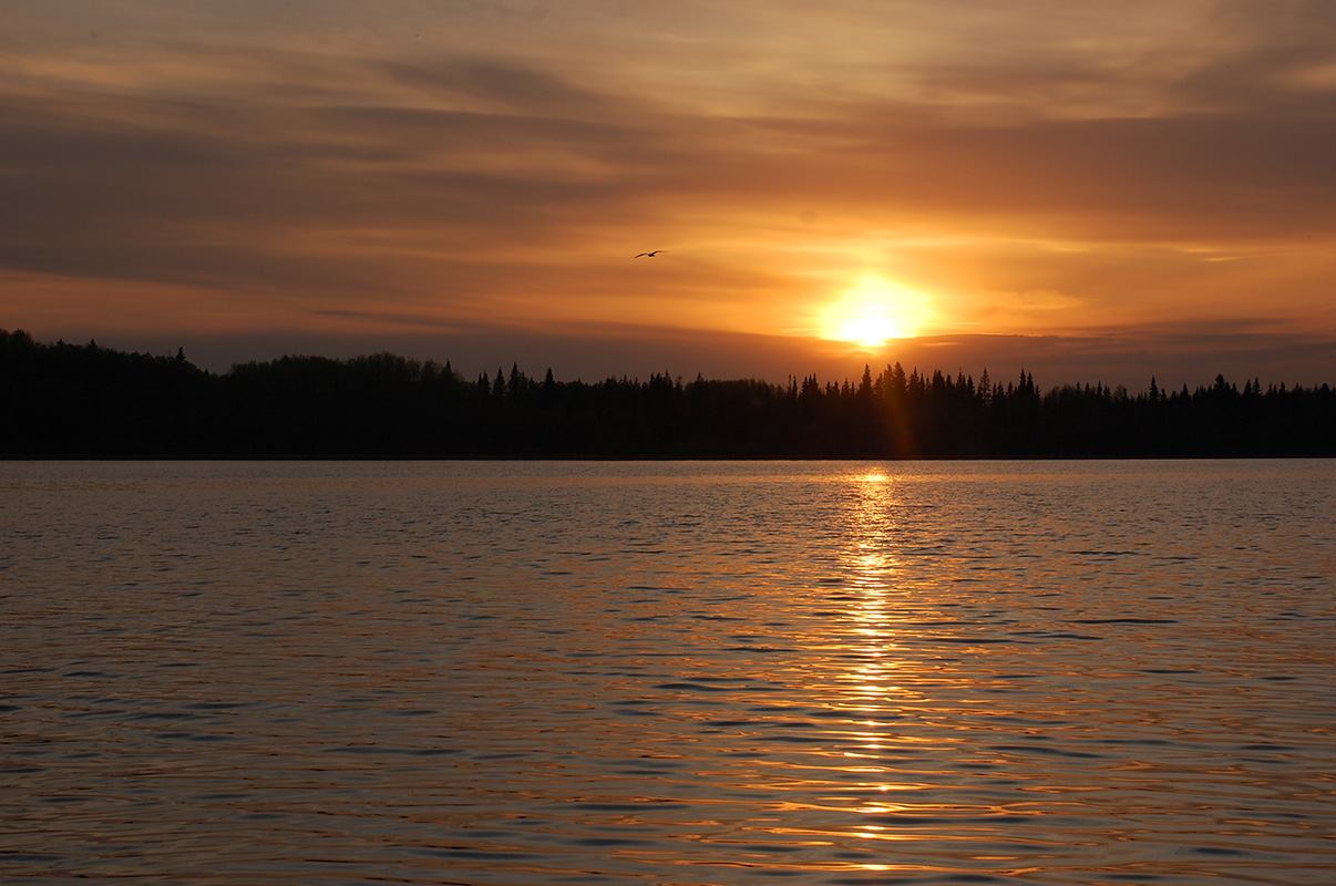 The sun glows orange as it sets over one of the Chain Lakes.