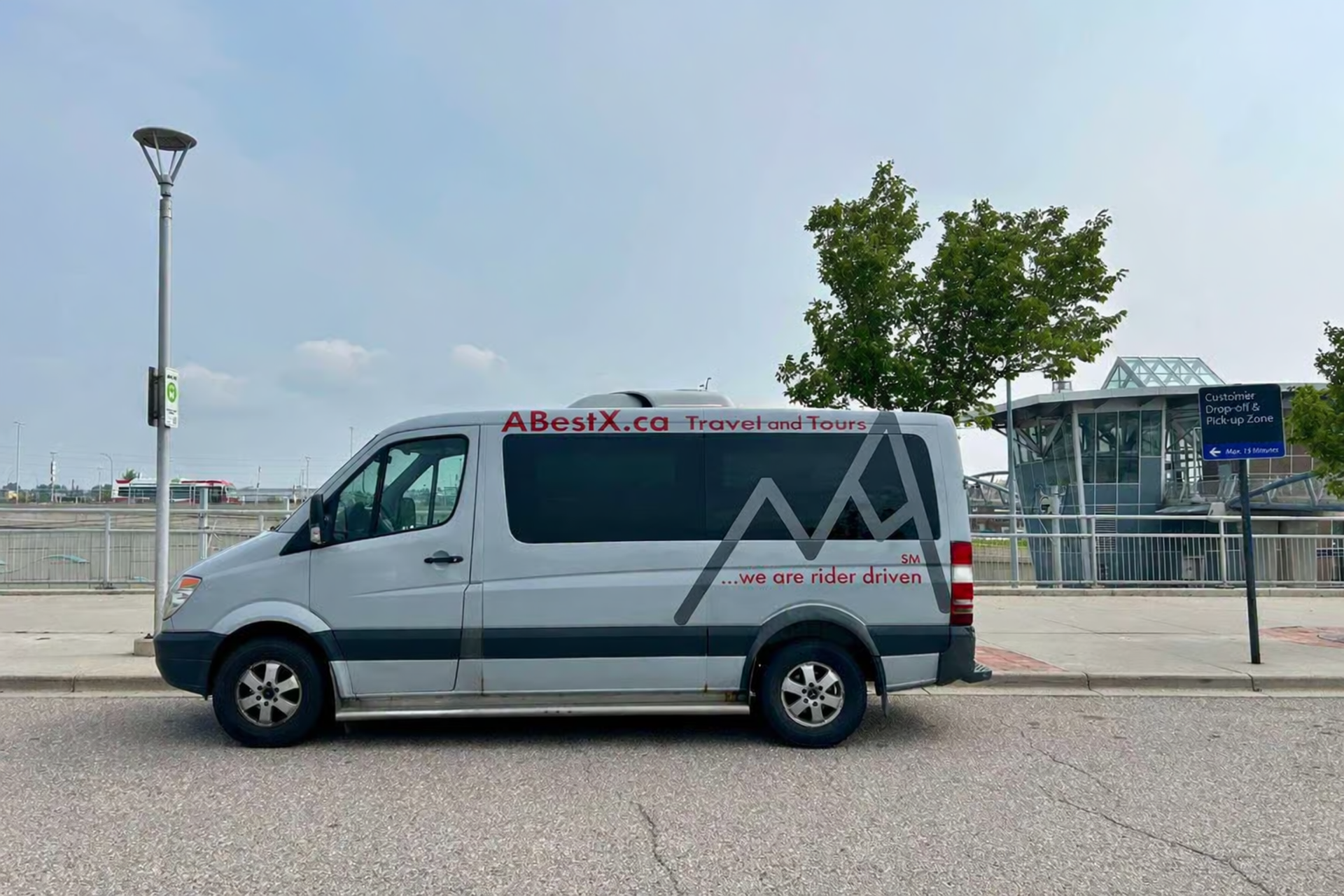 Passenger van with ABestX.ca Travel and Tours branding parked near transit station.