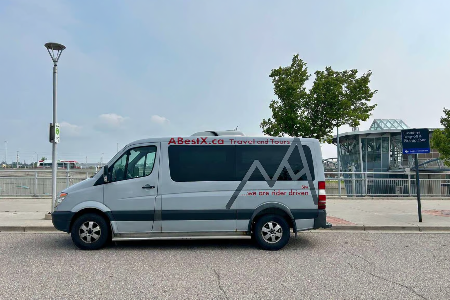 Passenger van with ABestX.ca Travel and Tours branding parked near transit station.