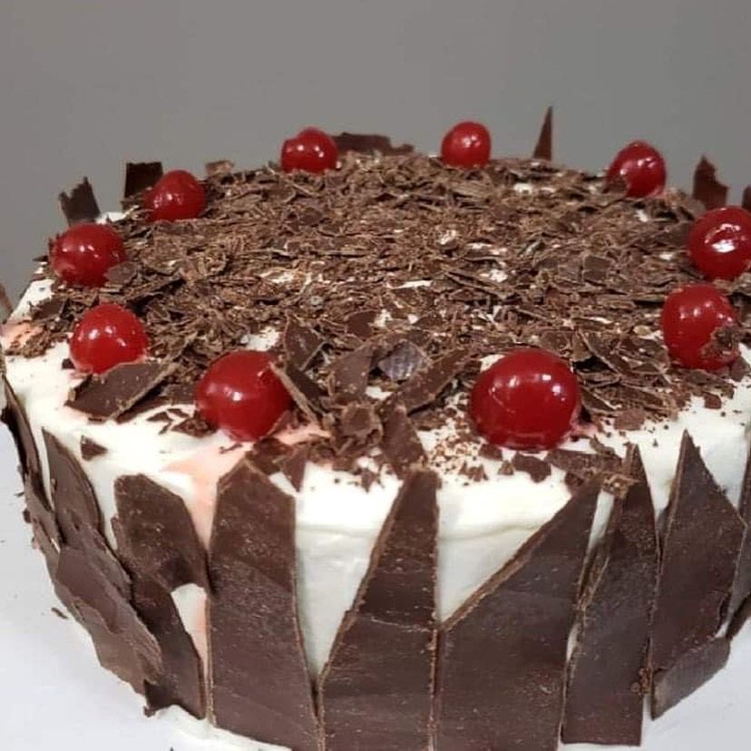 Black Forest cake with white frosting, chocolate shavings, and cherries on top.