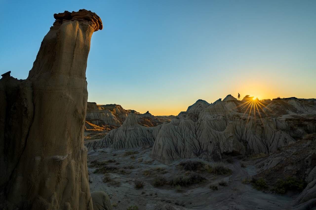 Rock hoodoos and ridges in badlands landscape with person silhouetted against sunset.