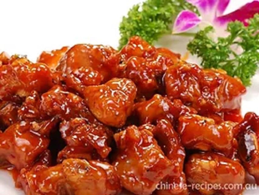 Glazed sweet and sour chicken garnished with parsley and a purple flower.