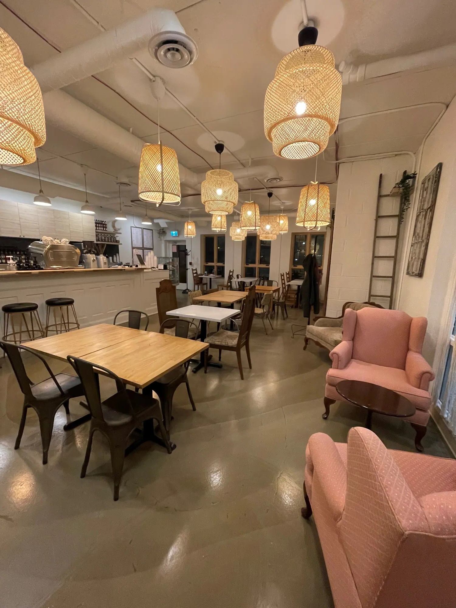 Cafe interior with wicker pendant lights, wooden tables, bar counter and pink armchairs.