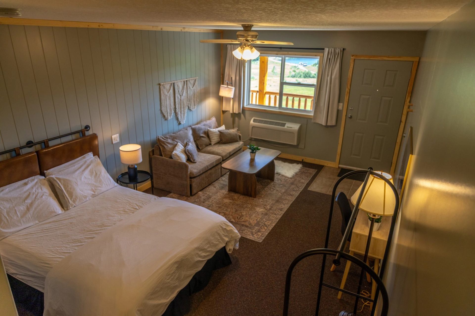 A ranch guest room with a bed, sofa, coffee table and window overlooking the balcony.