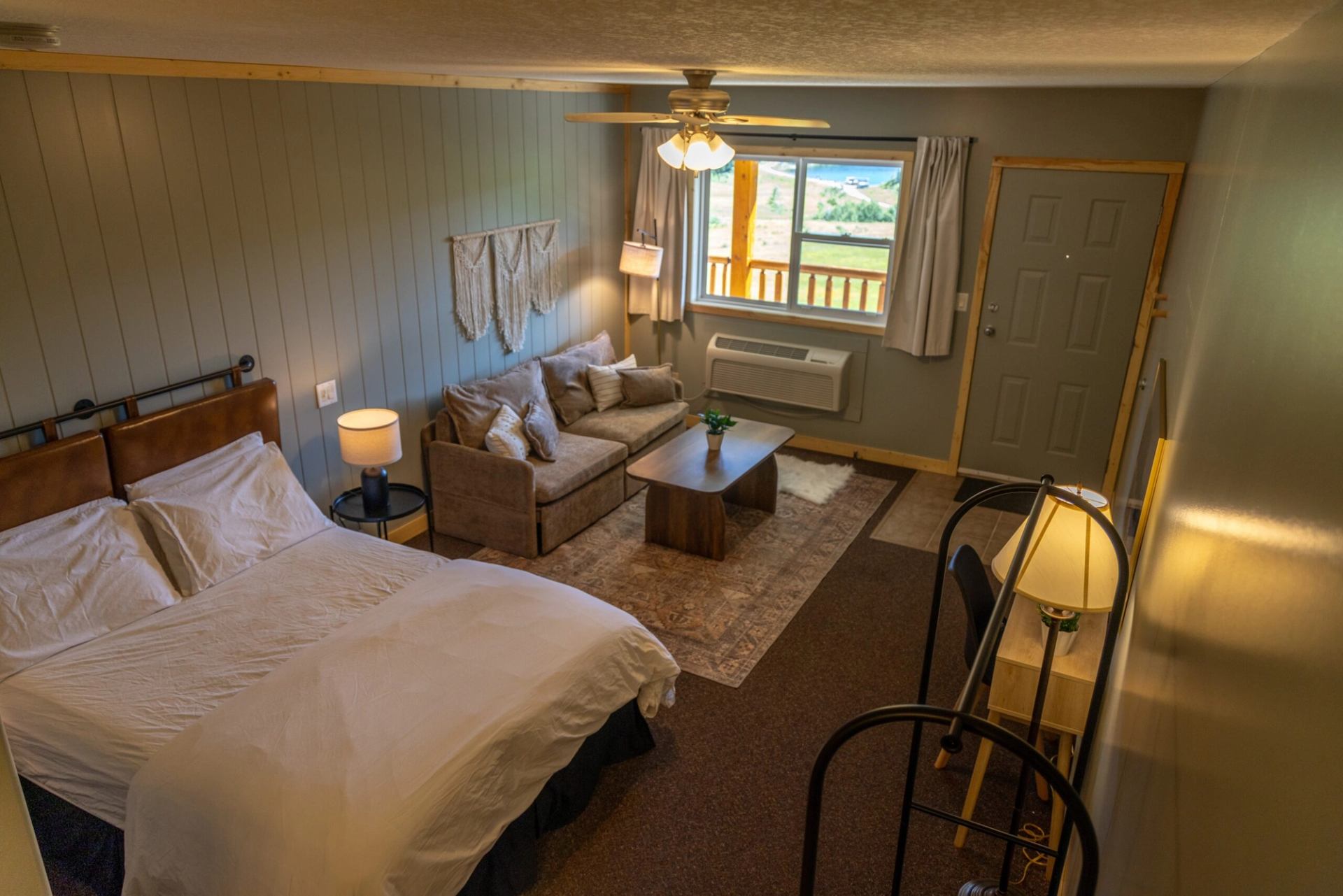 A ranch guest room with a bed, sofa, coffee table and window overlooking the balcony.