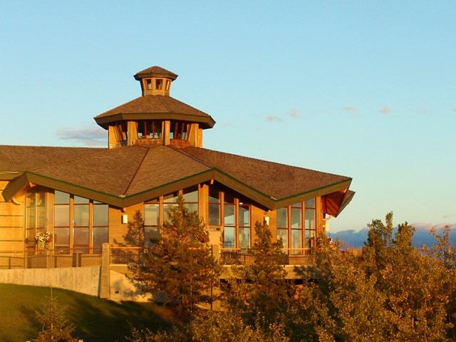 Front view of a large visitor center with a tower, green roof, and landscaped parking area.