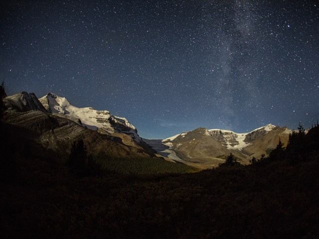 Night sky over a rocky mountain valley and trail in the Canadian Rockies.