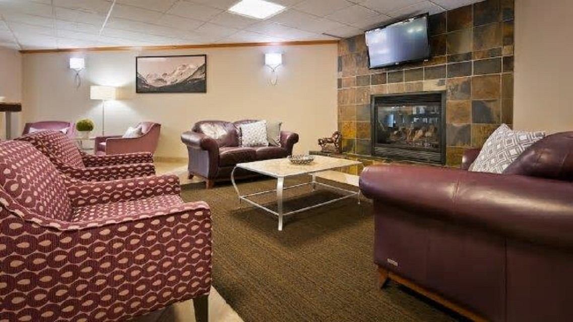 Hotel lounge with leather chairs, patterned sofas, and a wall-mounted TV by a fireplace.