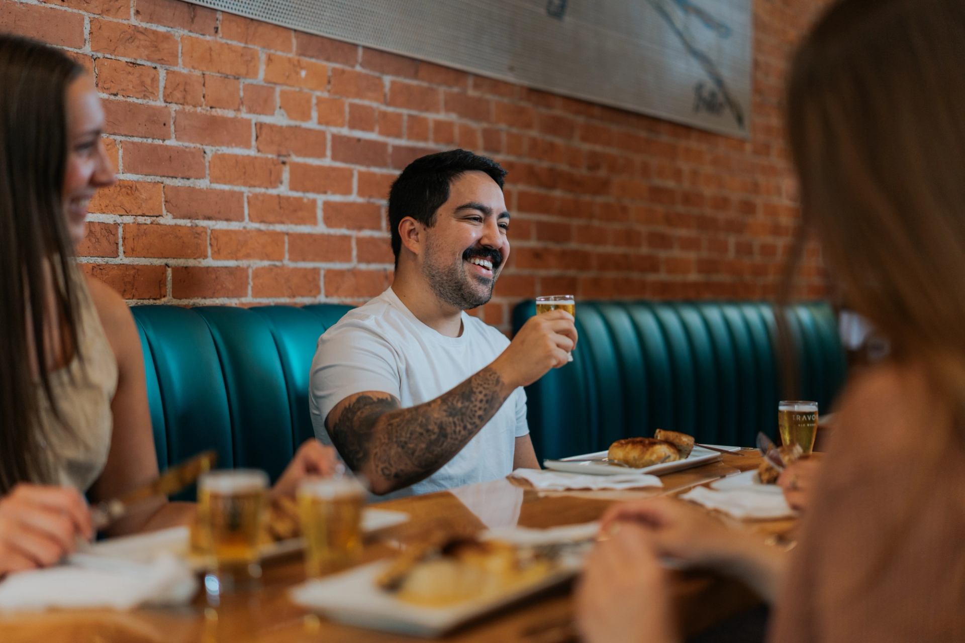 People enjoying drinks and food at a wooden table inside a cozy brick‑walled restaurant.