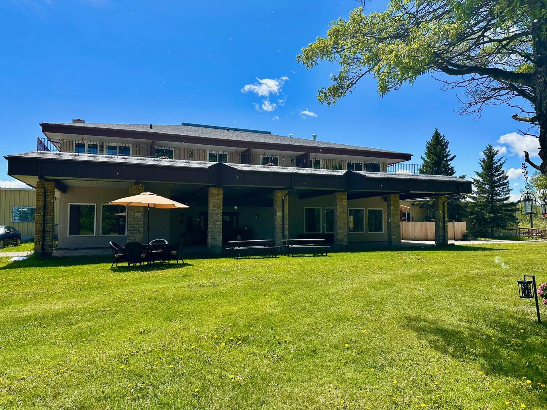 Two-storey building with covered patio, lawn chairs and umbrella on green grass.