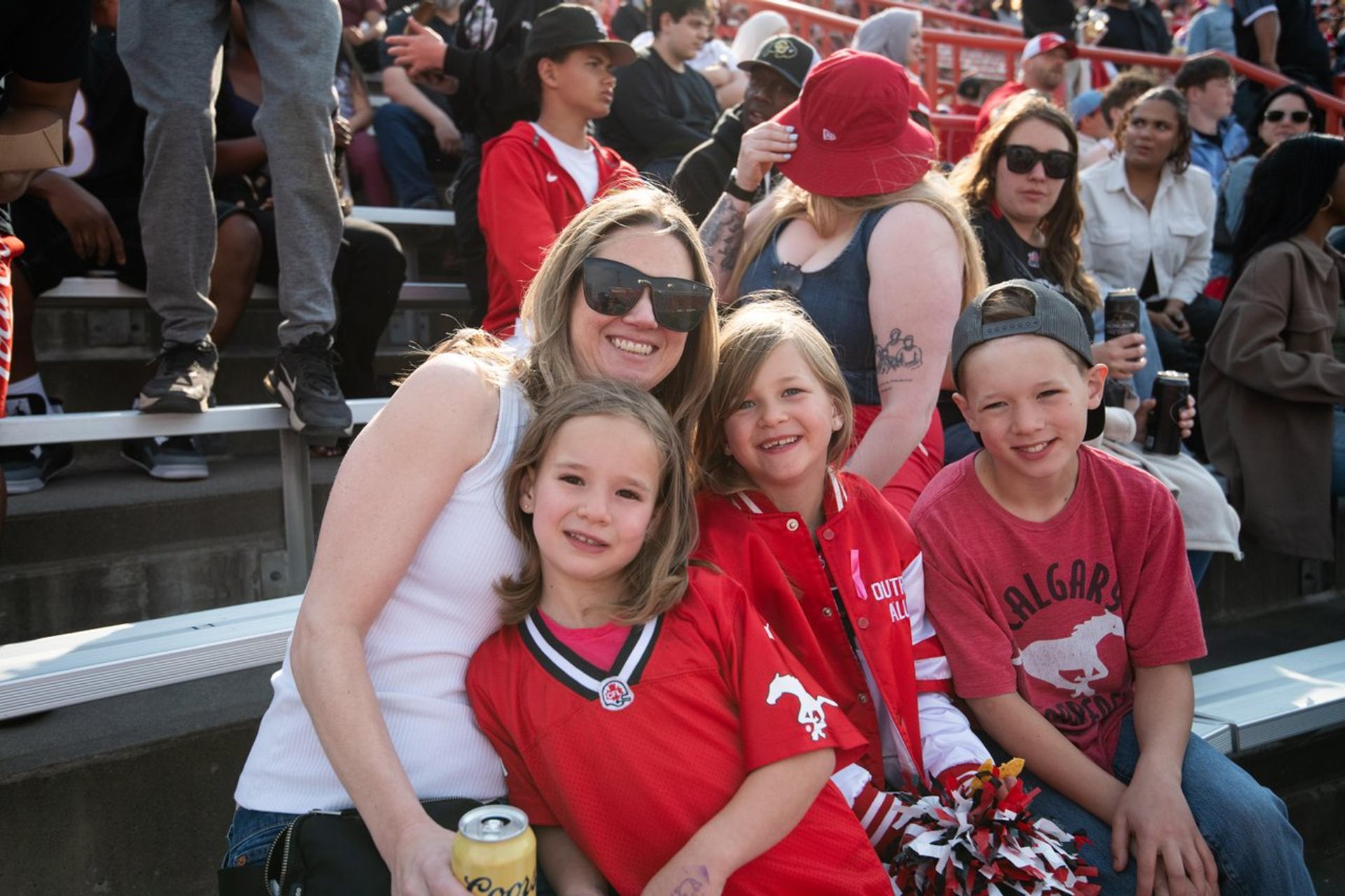 Spectators in red clothing pose together on crowded stadium bleachers.