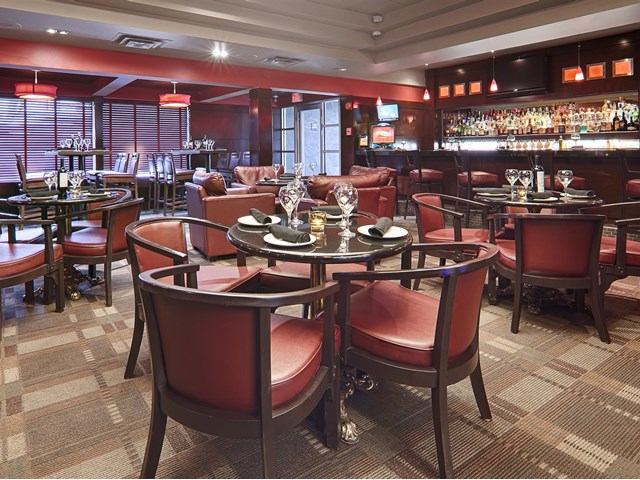 Elegant hotel restaurant with red chairs, round tables, and ambient lighting.