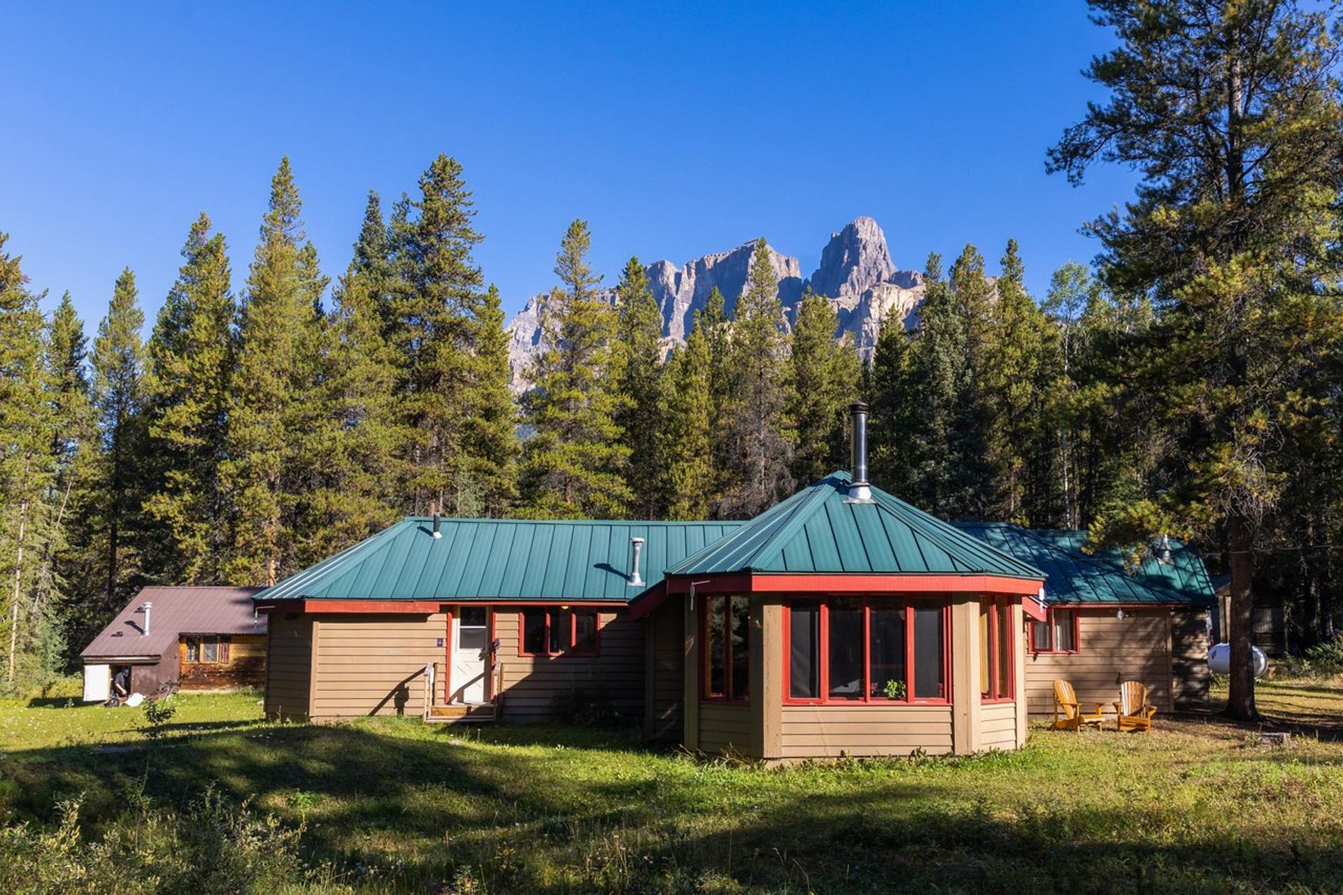 Rustic lodge with green roof and red windows, nestled in a forest of tall evergreens.