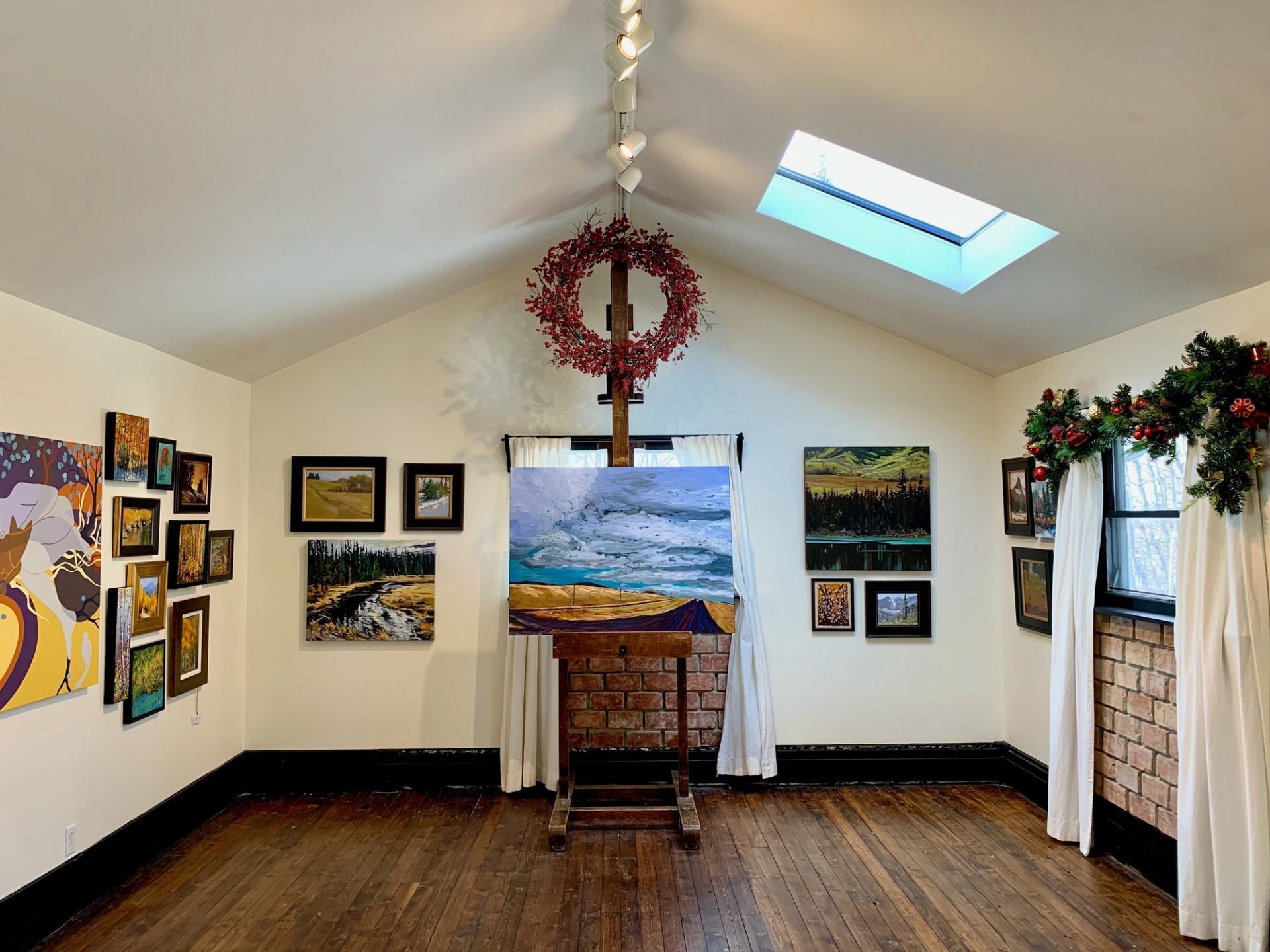 Art gallery with festive decor and diverse landscape paintings on display.