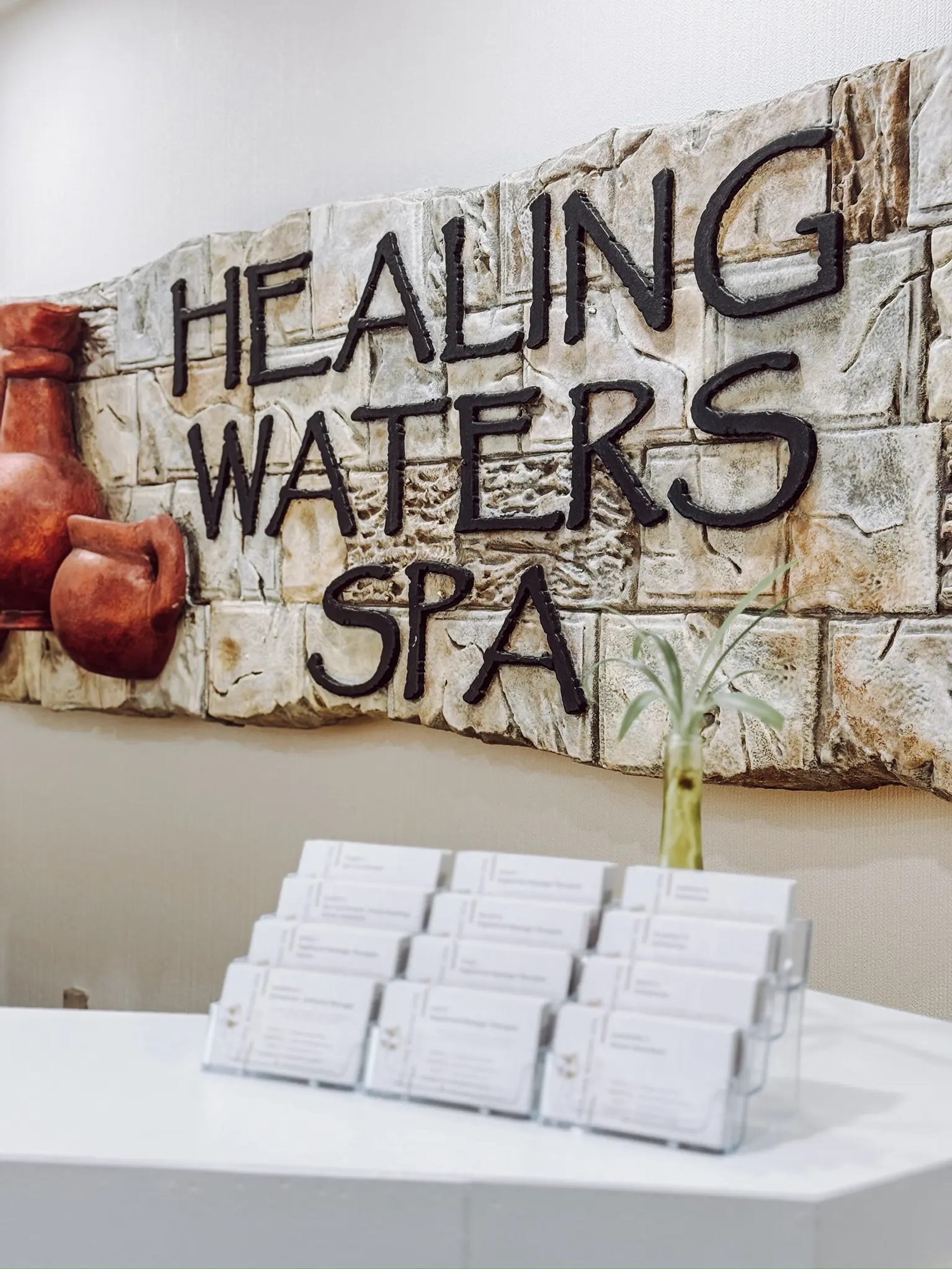 Stone wall sign reading “Healing Waters Spa” above a counter with brochures.