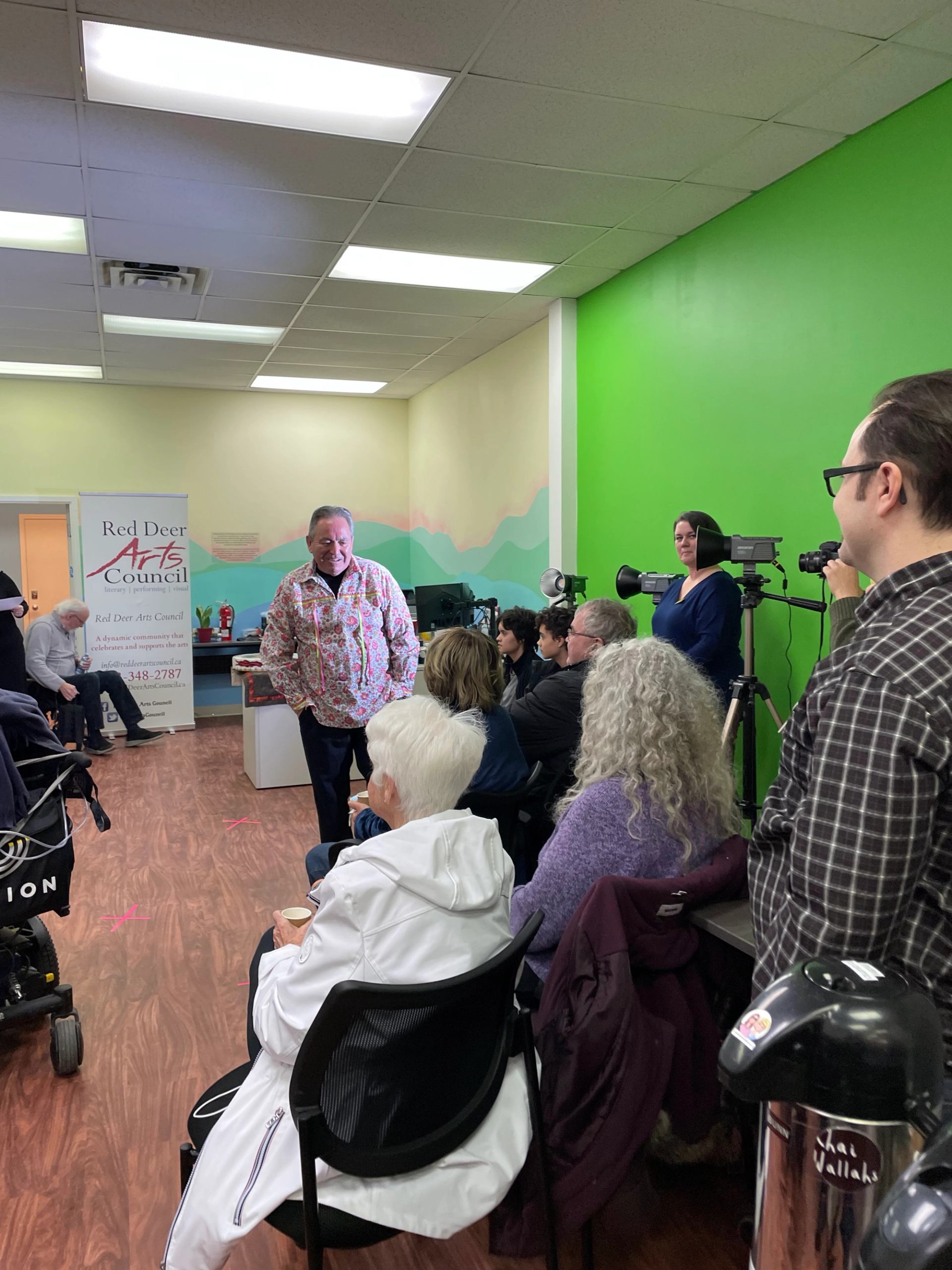 People chatting, cameras aimed at the stage, with a green-painted wall for visual effects.