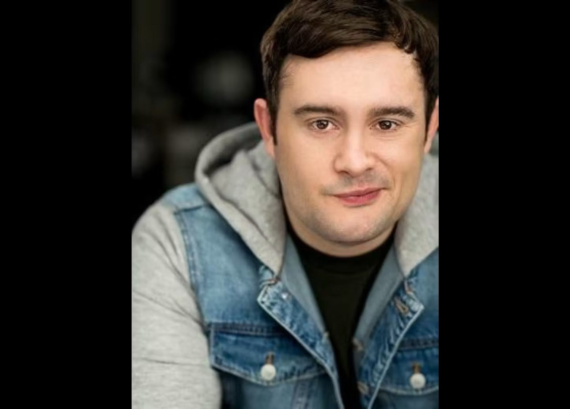 Person in denim jacket and hoodie with blurred background, facing the camera.