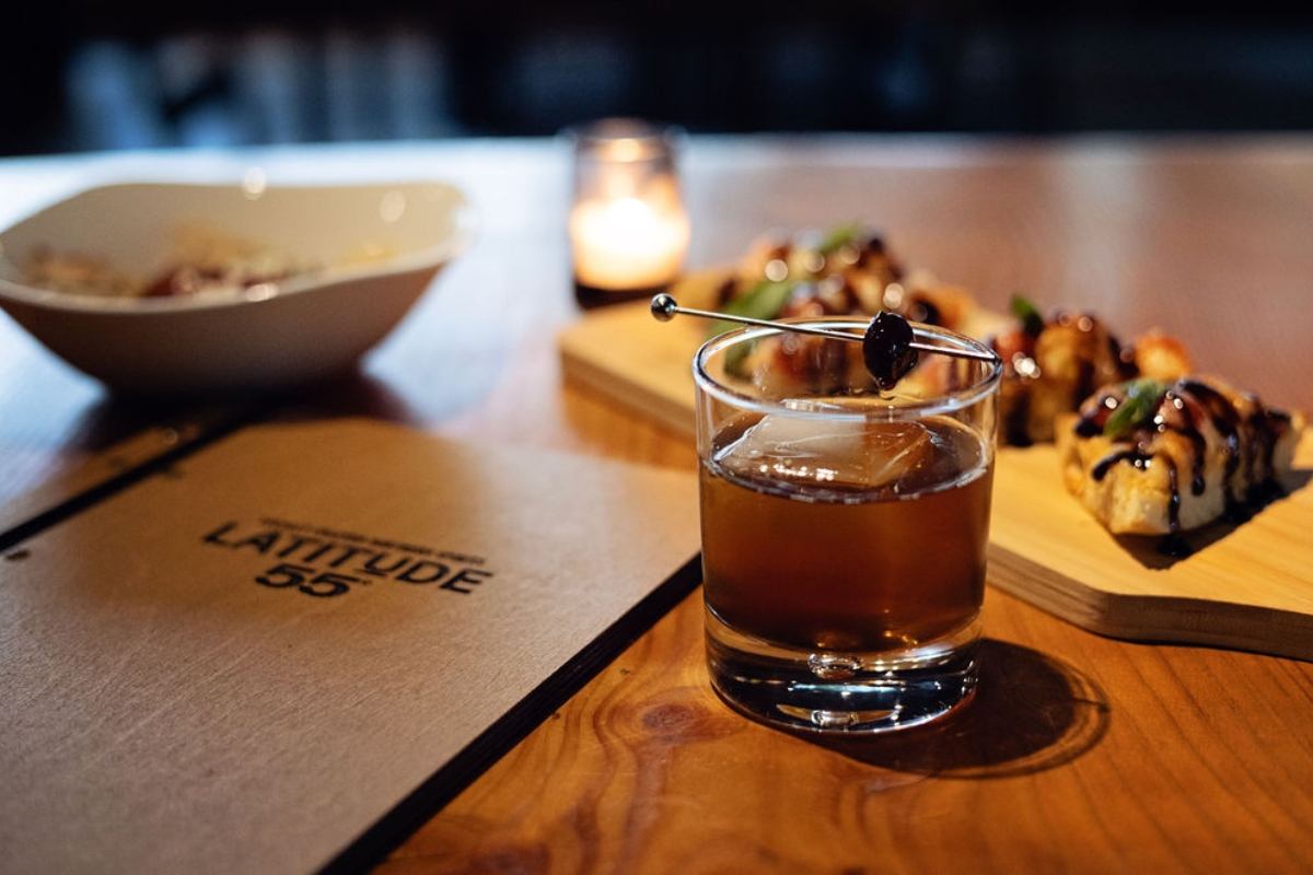 A cocktail, appetizers, and a candle on a wooden table at Latitude 55 Distillery and Lounge.