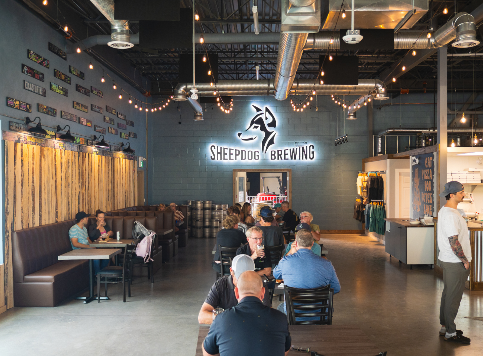 Sheepdog Brewing taproom with patrons seated beneath string lights and exposed ductwork.