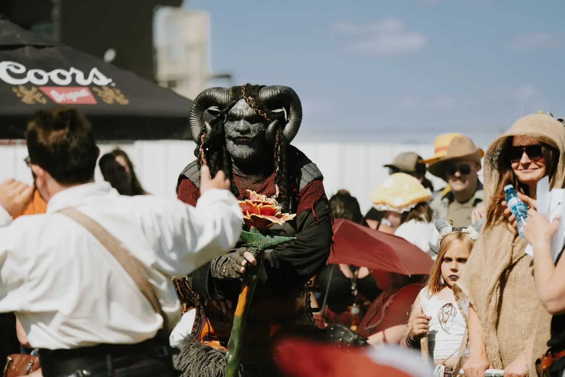 Person in horned mythical costume holding a staff at outdoor medieval-themed event.