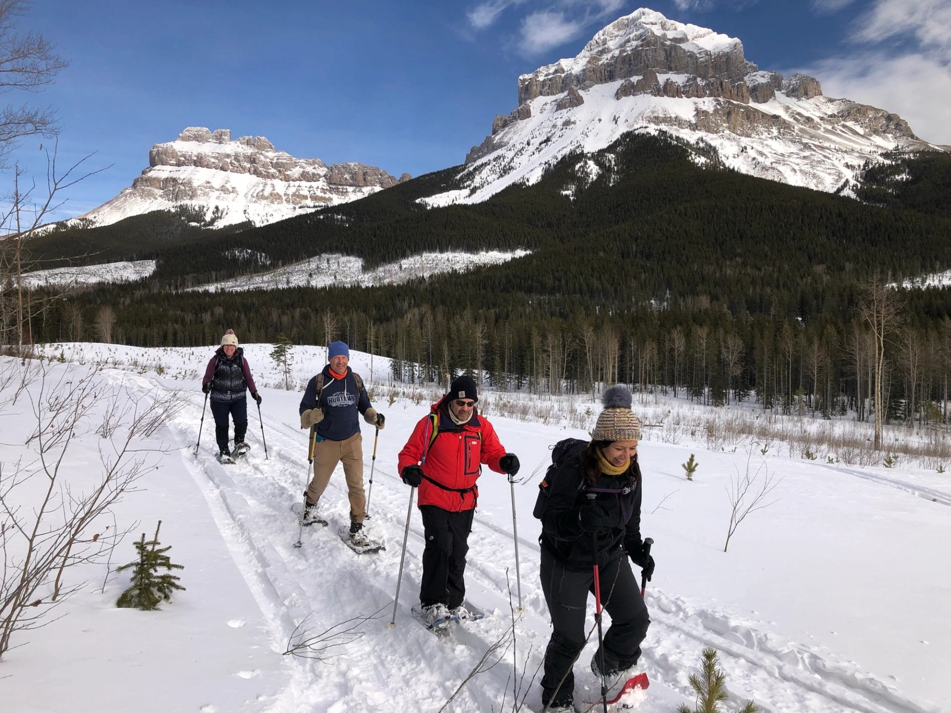 Group snowshoeing along a snowy trail with dramatic Rocky Mountain cliffs in the background.