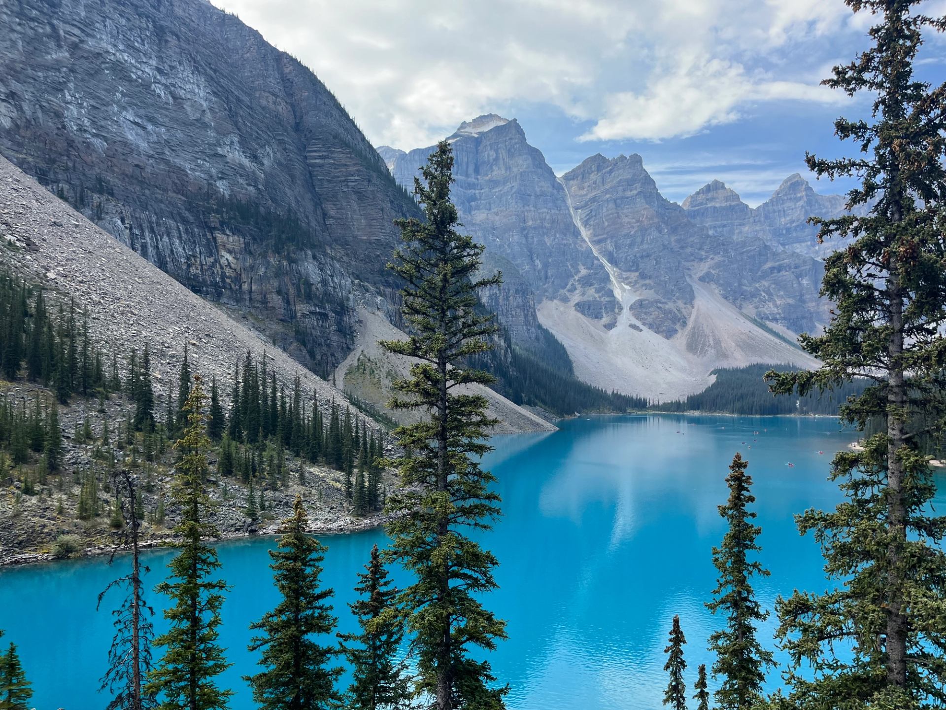 Turquoise mountain lake surrounded by steep rocky slopes and evergreen trees under cloudy sky.