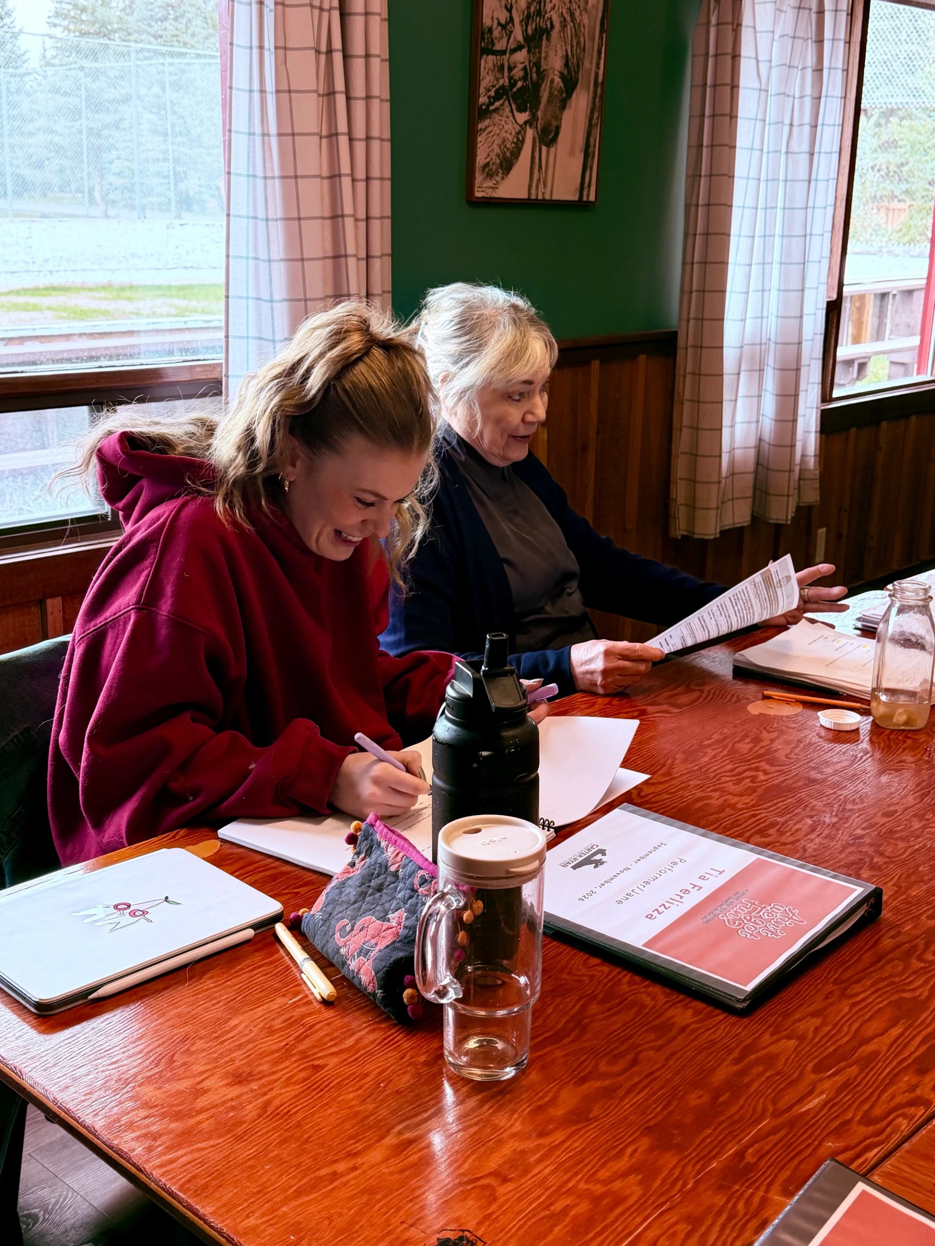Two people review documents and write notes at a wooden table.