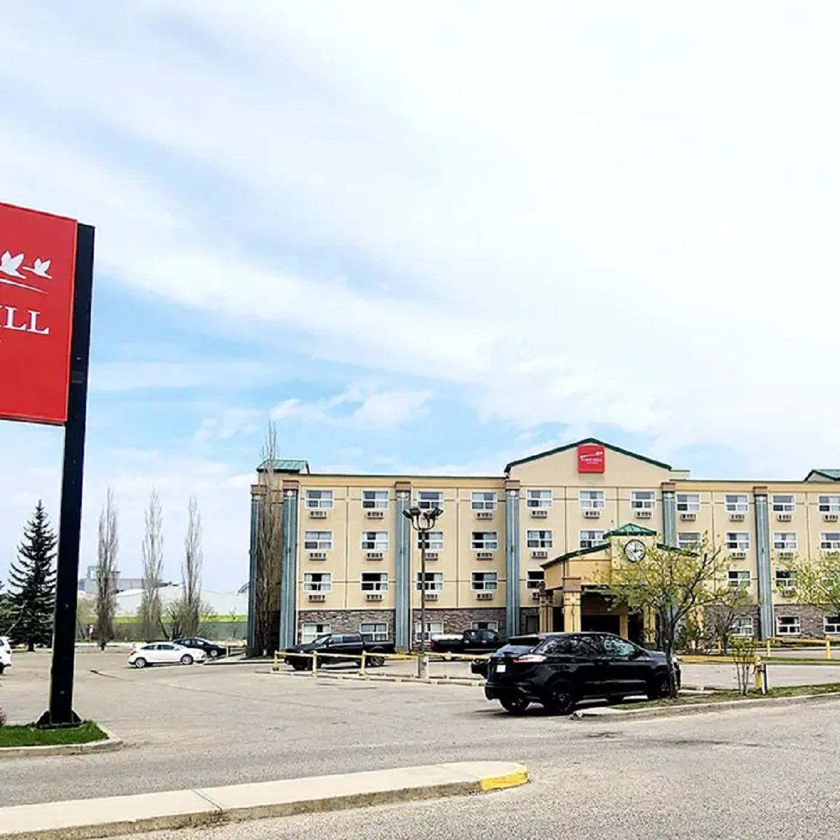 Exterior view of Park Hill Inn & Suite with parking lot and red sign under a clear sky.