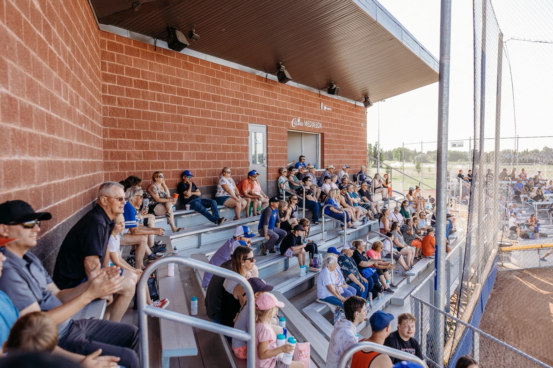 Spectators seated in covered bleachers watching a baseball game at the park.